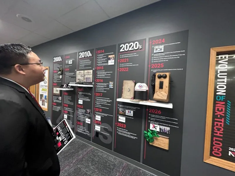 Kansas Broadband Office Deputy Director Visits Nex-Tech (1) Man viewing historical technology display at Nex-Tech exhibit in Kansas.